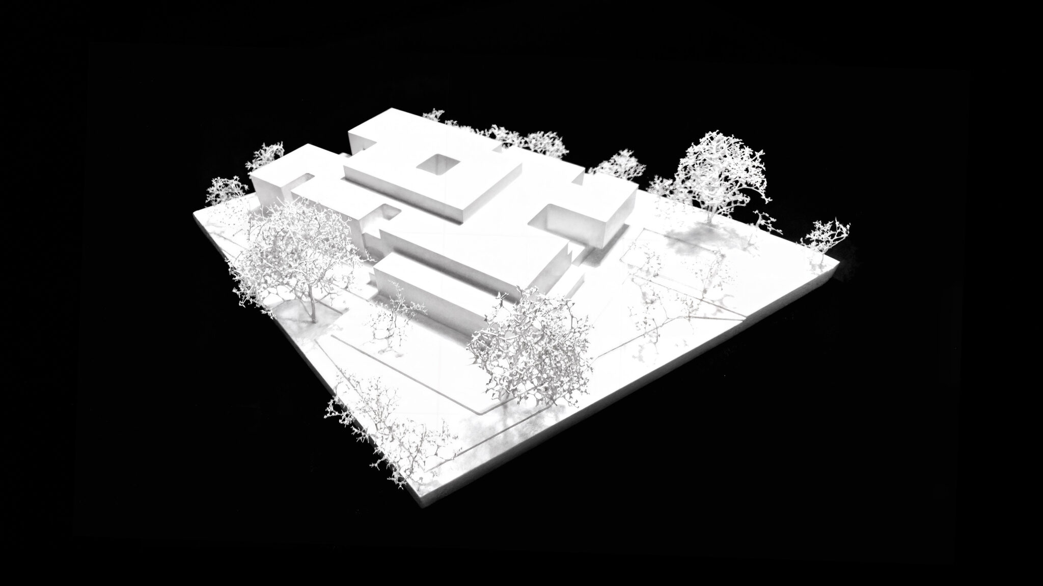 White architectural model of the Neue Mittelschule competition entry with building volumes and surrounding trees