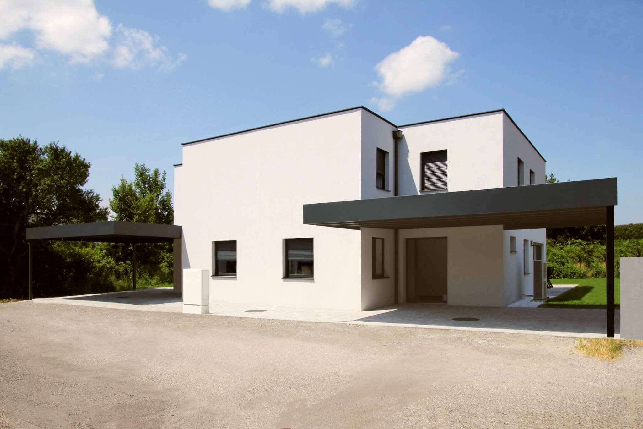 Completed duplex house with simplified carport and white façade, reflecting cost-saving adaptations.