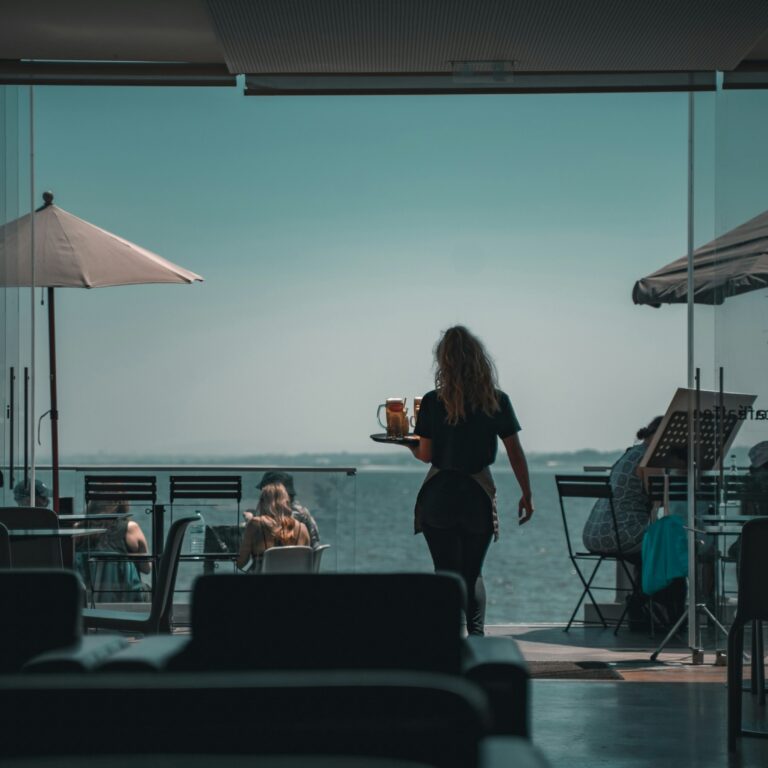 Waitress walking through a seaside restaurant with tables overlooking the water.